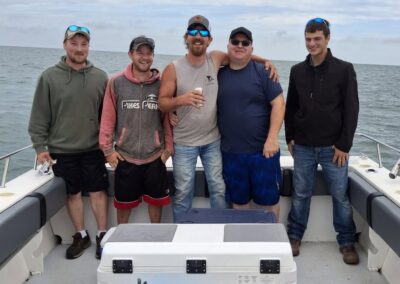 Five men are smiling and standing together on a boat under a cloudy sky
