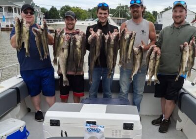 Five men stand on a boat smiling and proudly holding up large catches of fish after a successful fishing trip - foxyladycharterservice.com