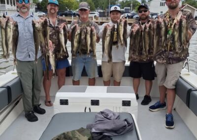 Six men stand side by side on a boat, smiling and holding up strings of freshly caught fish over a large white cooler