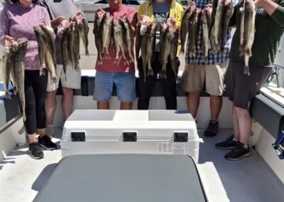 Six people stand on a boat under a clear blue sky, proudly holding up multiple strings of caught fish above a large white cooler