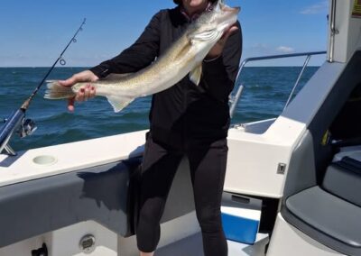A woman stands on a boat under a clear blue sky, smiling as she holds up a large walleye she caught - foxyladycharterservice.com