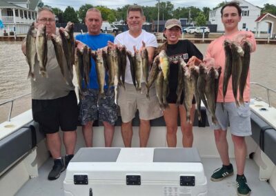 Five smiling individuals stand in a line on a boat, proudly displaying a large catch of fish strung across their hands - foxyladycharterservice.com